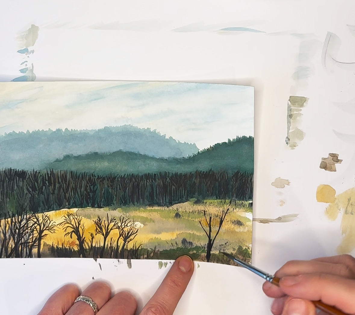 A photo of Jennifer Millard's hands while she paints a watercolor of the trees and hills in eastern Kentucky.