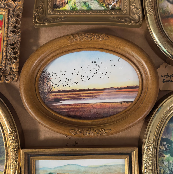 Example of a giclee print of birds lifting out of a tree and taking flight, framed in an oval vintage wood frame.