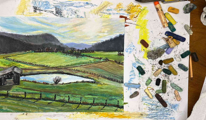 A photo of the artist's table where she uses oil pastels to depict this view off Red Lick Road in Kentucky.