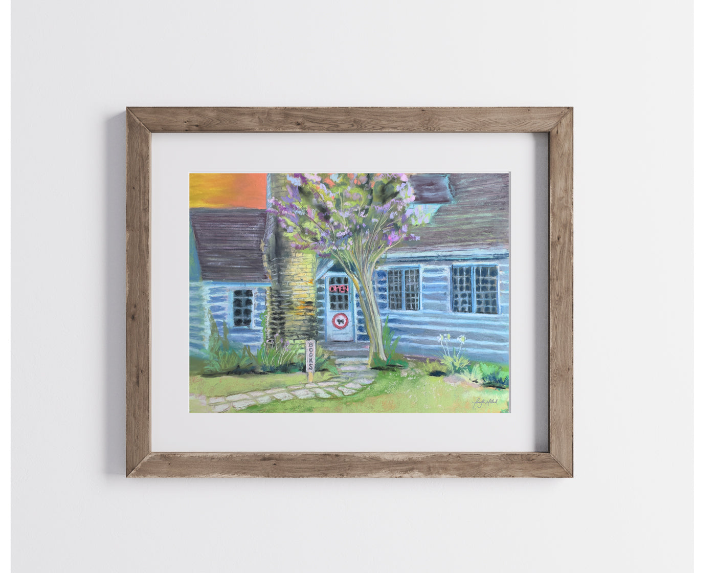 A soft pastel print of The Taleless Dog Bookstore in a natural wood frame with a white mat.