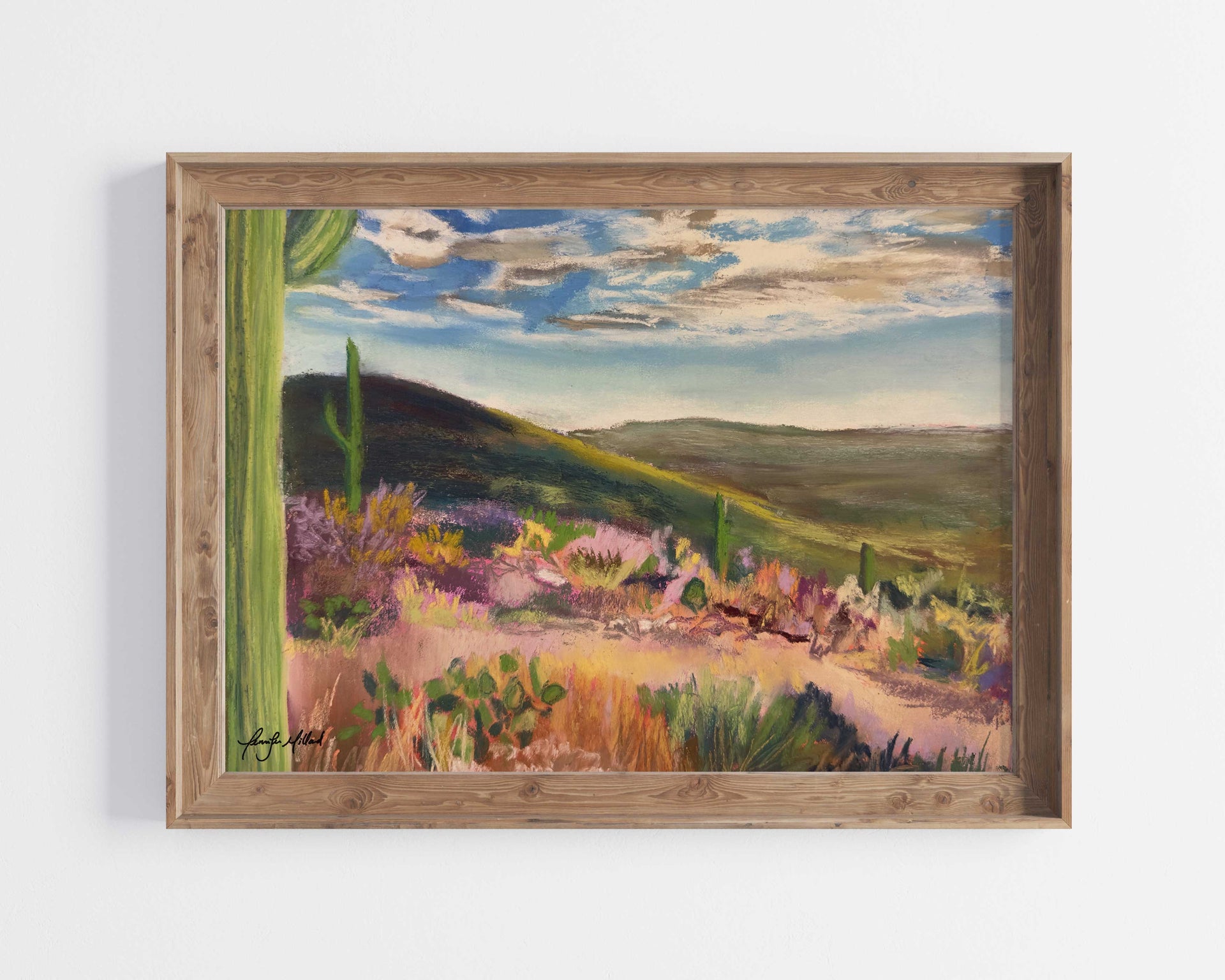 A print of a colorful painting of a desert vista with rolling hills displayed in a natural wood frame.